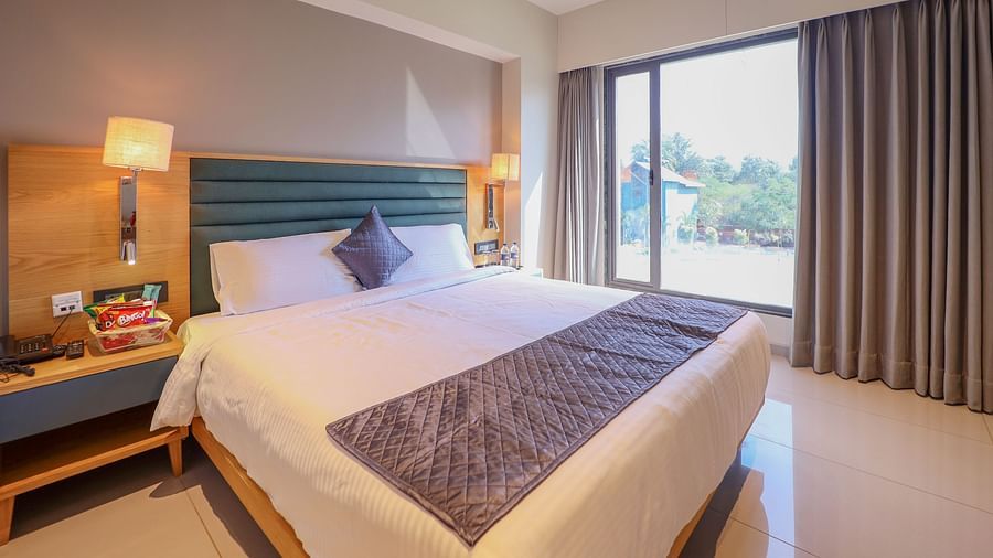 Bedroom with double size bed, bedside lamp on either side, and a balcony  attached - Pride Resort Ambaji